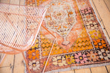 Distressed Oushak rug corner showing worn tangerine, saffron, and blush curvilinear floral motifs.