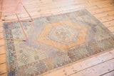 Distressed Oushak rug corner: faded orange field, diamond border, and hook-and-latch motif.