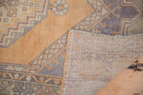 Distressed Oushak rug's faded burnt orange pile, geometric pattern, and hand-knotted foundation.