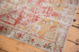 Distressed Oushak rug corner featuring cherry red, saffron, silver floral border, and exposed foundation.