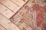 Distressed Oushak rug corner revealing worn pile, fuchsia, cherry red, and silver border motifs.