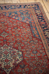 Angled view of an antique Bijar rug's corner with a red Herati motif and detailed navy border.