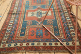 Geometric madder red and teal patterns on an antique Farchalou Kazak Caucasian rug's tattered edge.