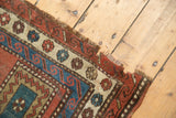 Hand-knotted antique Caucasian rug's geometric red, teal, ivory borders and tattered fringe.