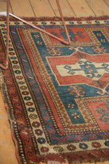 Antique Caucasian rug detail: geometric patterns in madder red, teal, ivory, showing tattered edge wear.