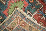 Antique Heriz rug runner corner showing geometric motifs, worn low pile texture, and tattered fringe.
