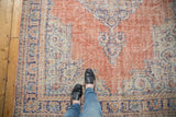 Distressed Oushak rug's pale brick red field with blue and ivory curvilinear motifs.