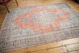 Distressed Oushak carpet corner with pale brick red field, navy border, and visible wear.