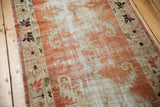 Distressed texture of vintage Turkish Oushak runner, muted brick red and antique ivory field, dark floral border.