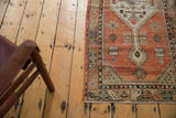 Faded brick red and seafoam geometric motifs on a distressed Oushak rug runner corner.