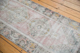 Distressed Oushak runner section displaying worn pile and soft blush, ivory floral patterns.