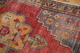 Distressed Oushak rug detail: stepped tangerine spandrel, red field, and slate blue floral elements.