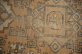 Distressed Melas rug close-up: light bronze, pale green geometric patterns with worn texture.