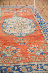 Textured distressed Oushak runner showing worn orange-red pile, sky blue, and ivory floral pattern.