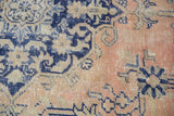 Distressed Oushak rug's faded apricot, dusty blush, navy, and beige patterns with even wear.