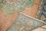 Distressed Oushak rug corner showing blush and mint pile over its woven reverse.