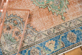 Distressed Oushak rug detail: blush peach field, sky blue border, and faded curvilinear motifs.