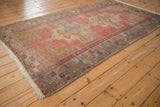 Faded cinnabar red distressed Oushak rug with ivory rams horn medallion, plum, and blue.
