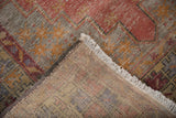 Distressed Oushak rug's folded corner, showing fringe and marked hand-knotted reverse.