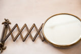 Beveled glass and darkened brass frame of an antique accordion shaving mirror.
