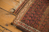 Antique Belouch rug corner showing madder root red field, zig-zag border, and tattered fringe.