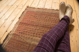 Antique Belouch rug's worn madder red boteh pattern and tattered fringe beneath resting boots.