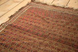 Angled close-up of antique Belouch rug, highlighting madder root red boteh pattern, evident wear to hand-knotted pile, and tattered edge.