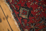 Fringed edge and worn pile of the antique Lilihan mat, featuring cherry red, teal, navy floral motifs.