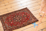 Angled view of a vintage Farahan Sarouk rug with cherry red floral field and central medallion.