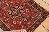 Vintage Farahan Sarouk rug corner with cherry red field, intricate floral details, worn fringe.