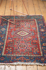 Corner of an antique Karaja rug with tattered fringe, geometric blue border, and cherry red field.