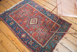 Corner of antique Persian Karaja rug with blue geometric border and visible fringe loss.