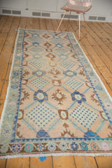 Distressed Oushak rug with pale blush, faded blue lattice, and checkered floral motifs.