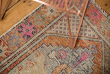 Distressed Oushak rug corner with vibrant hot pink, orange, and beige geometric motifs.