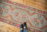 Distressed vintage Oushak runner with faded blue, bright rust, and hot pink stepped medallion.