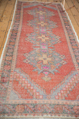 Distressed vintage Oushak rug runner showing faded cinnabar field and checkered spandrel.
