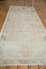 Distressed Oushak runner end, pale sand geometric medallion, barber pole border, worn texture.