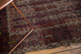 Antique Belouch rug's geometric floral bands, dark palette, and worn tattered edge.