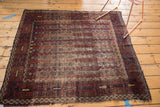 Antique Belouch rug corner: striped flowers, channel motifs, geometric border, frayed edge.