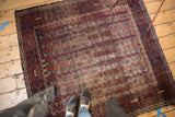 Antique Belouch rug corner, highlighting tattered edge, navy geometric border, and faded floral motifs.