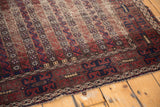 Antique Belouch rug's decorative border, tattered edge, and etched chocolate brown patterns.