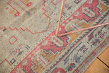 Faded cinnabar border and geometric patterns on a distressed Oushak rug pile.