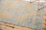 Distressed vintage Oushak runner's textured pile in pale saffron, slate blue, with fringe.