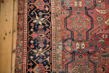 Detail of the Vintage Heriz carpet's dark border with pinwheel motifs, and cherry red field with foundation showing.