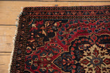 Antique Farahan Sarouk rug corner, with visible tatter and deep navy, cherry red motifs.