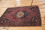 Corner of an antique Farahan Sarouk rug showing significant end loss and floral motifs in cherry red, navy, and ivory.