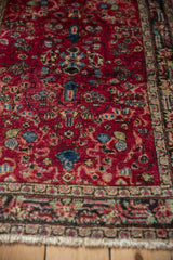 Angled view showing the worn, low pile and white knot heads of a vintage red Persian rug.