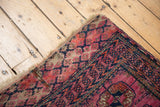 Antique Turkmen rug corner with fuchsia, navy, rust geometric borders, visible patch, and side tatter.