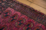 Antique Turkmen rug with fuchsia field, navy elephant footprint guls, and tattered edges.