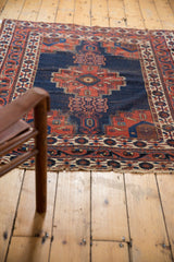 Antique Afshar rug corner: geometric borders, dark blue field with potted plants, tattered end.